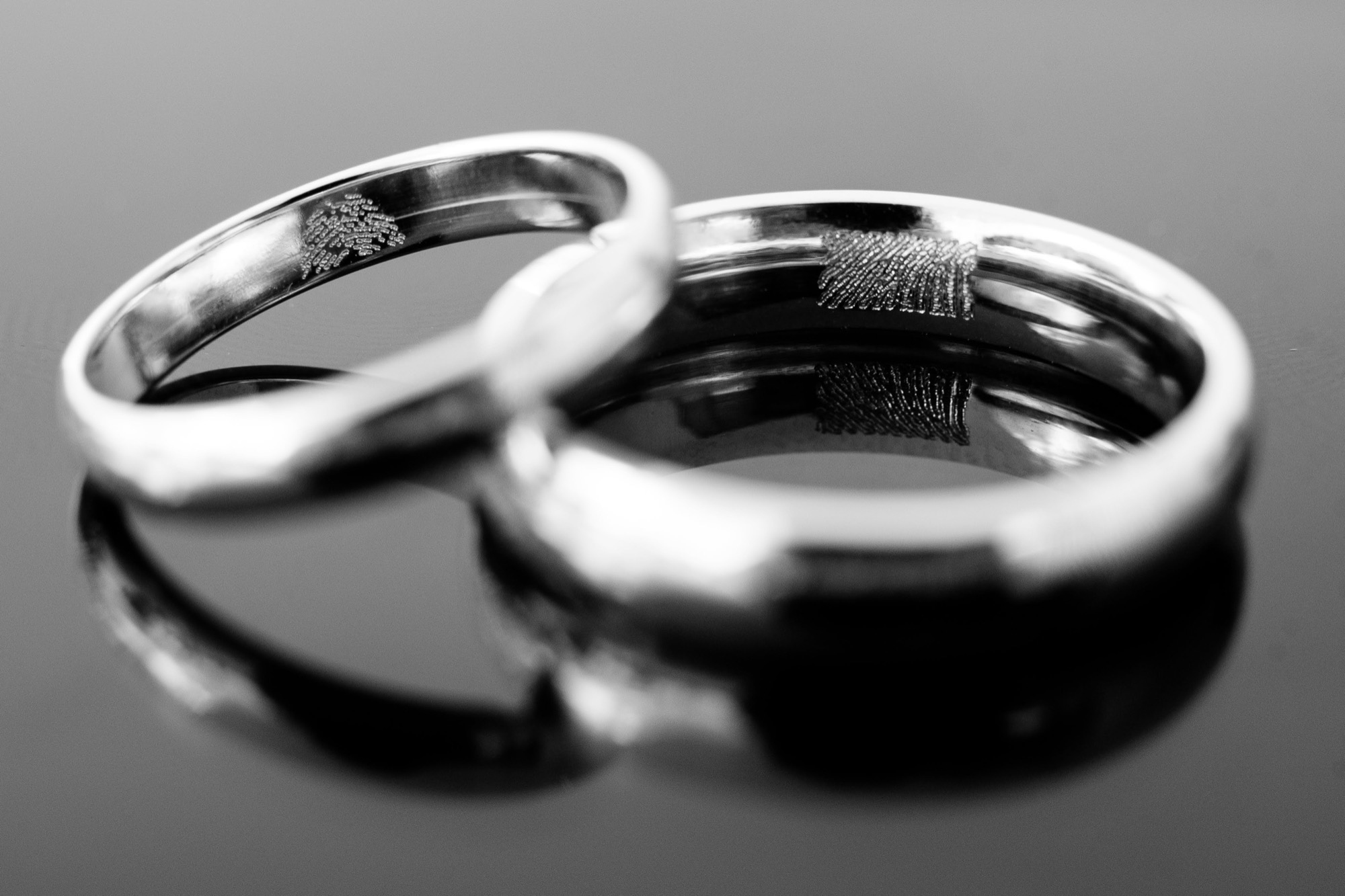 A pair of gold wedding bands, each engraved inside with a partner's fingerprint